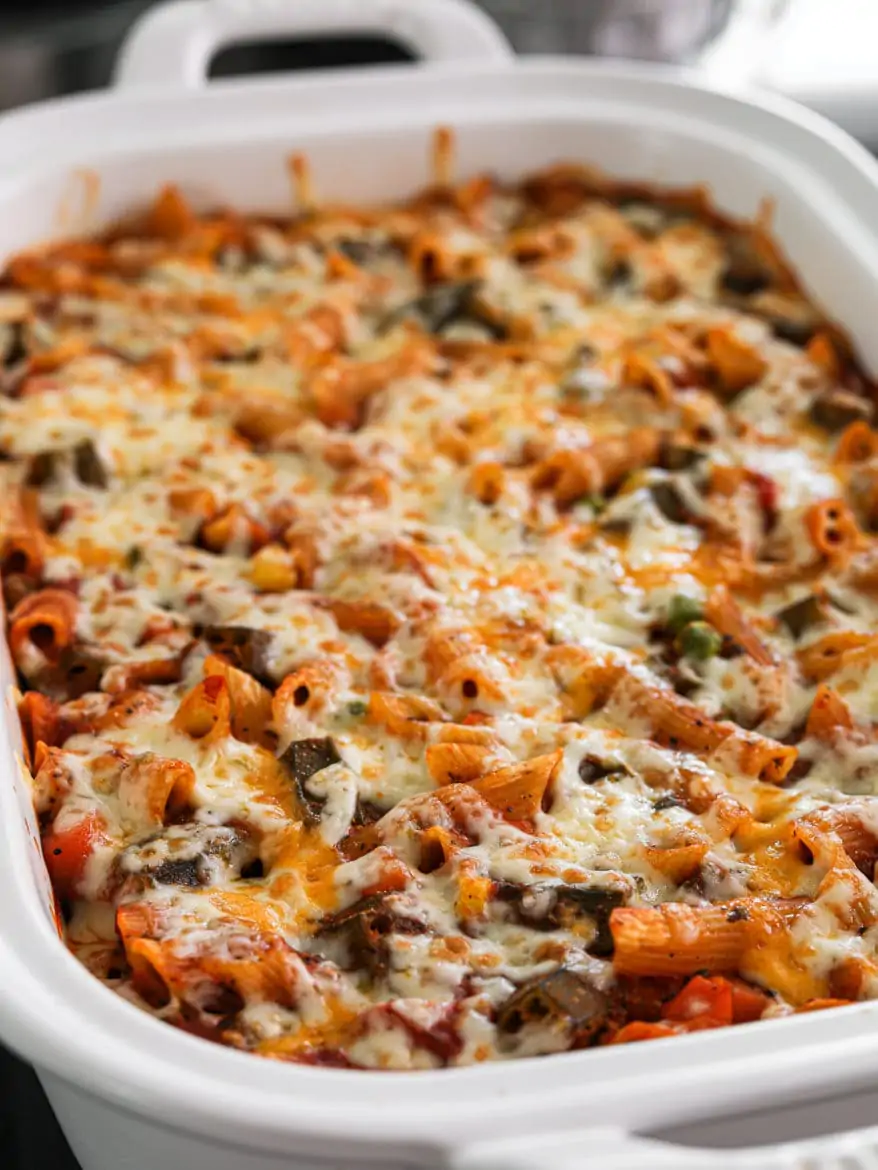 a white rectangular casserole dish with pasta bake made with mixed vegetables topped with melted cheese on - close up shot