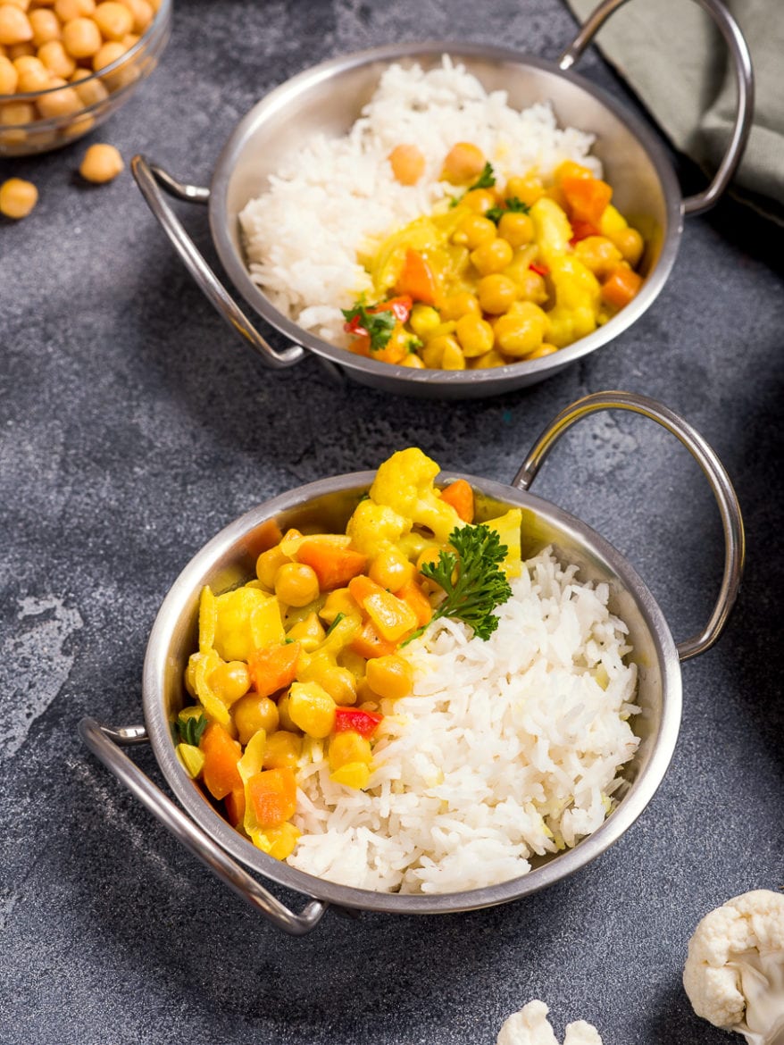 Vegetarian curry with cauliflower and chickpeas served in metal bowls with rice, healthy vegan food, indian cuisine