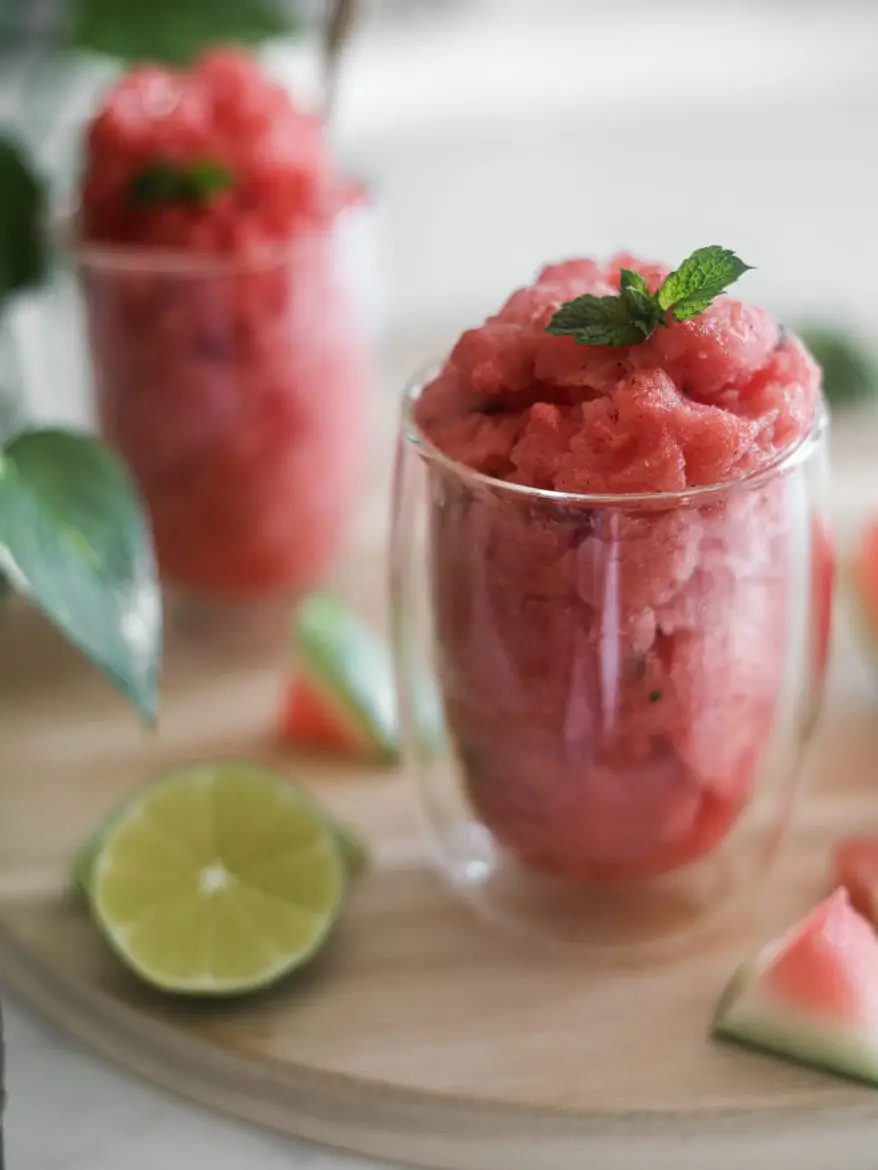 close up of watermelon slushie in 2 glasses with a lime slice next to them