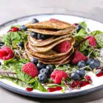 Vegan chickpea pancakes served in plate with green salad young beetroot leaves, sprouts, berries, berry sauce over grey kitchen table. Close up. Healthy eating