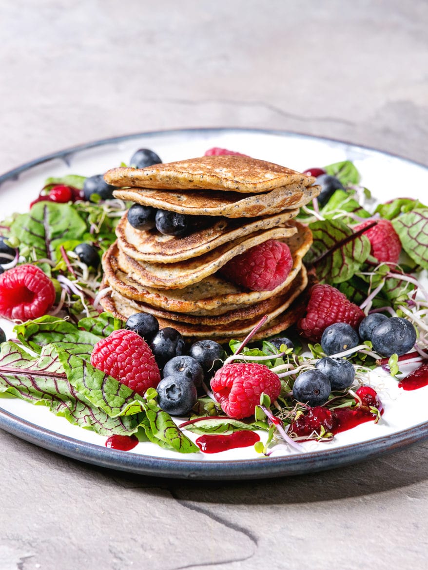 Vegan chickpea pancakes served in plate with green salad young beetroot leaves, sprouts, berries, berry sauce over grey kitchen table. Close up. Healthy eating