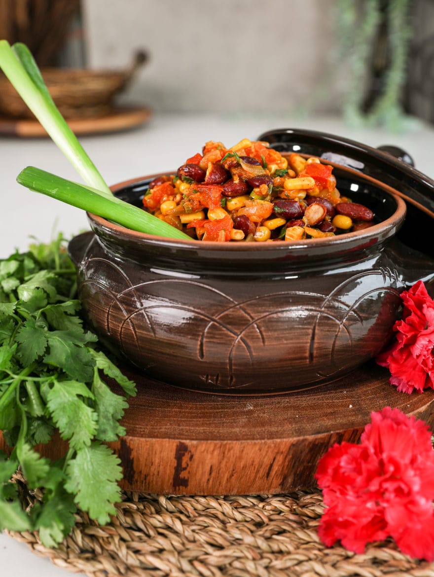 a brown clay pot filled to the top with githeri (Kenyan beans and corn) with 2 stalks of scallions sticking out. Angled shot.