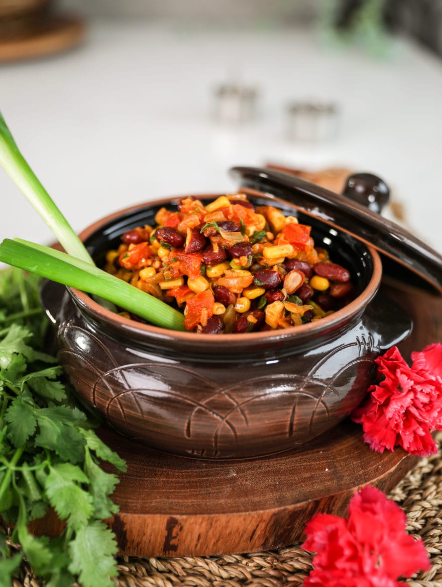 a brown clay pot filled to the top with githeri (Kenyan beans and corn) with 2 stalks of scallions sticking out. Angle shot