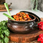 a brown clay pot filled to the top with githeri (Kenyan beans and corn) with 2 stalks of scallions sticking out. Angles shot on a kitchen counter.