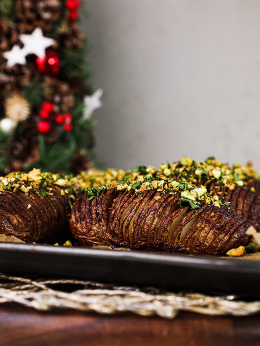 side view of thinly sliced hasselback potaotes topped with nut-herb crumble with festive decorations in the background