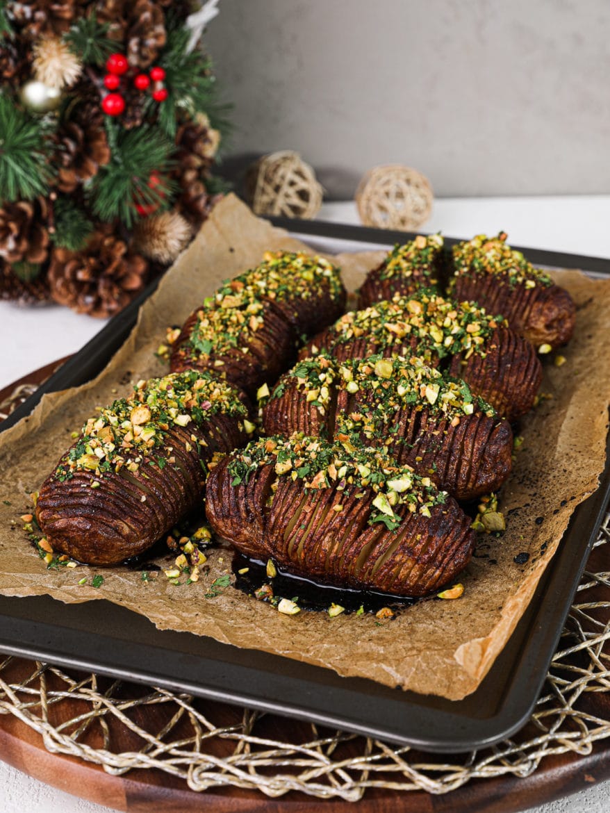 baking tray of baked hasselback potatoes topped with a nutty crumble with a Christmas tree in the background