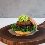 a burger on brioche bread with a base of lettuce, grated beets and finally topped with a green slaw. Placed on top of a wooden board
