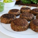 lentil burger patties arranged on a white plate with lettuce and burger add-ins the background.