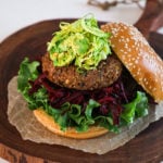 close up shot of a burger made of lentils that's on a bed of greens and beetroot and topped with a green slaw
