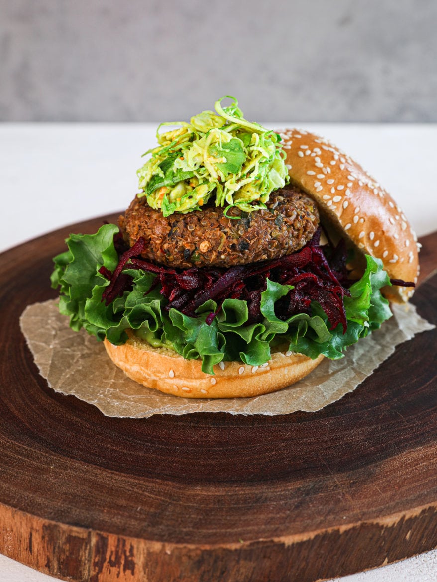 perspective shot of a lentil veggie burger on a bed of greens and beetroot and topped with a green slaw