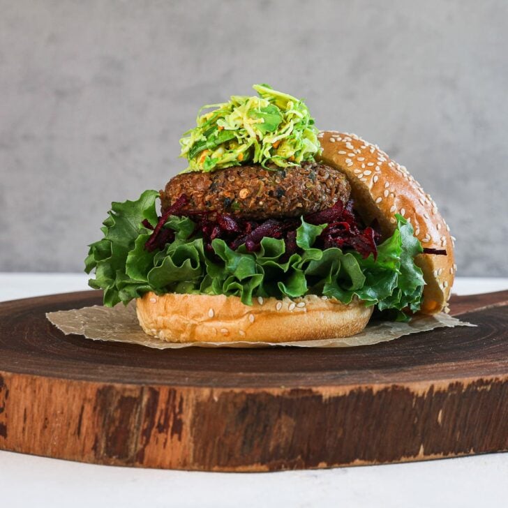 perspective shot of a lentil veggie burger on a bed of greens and beetroot and topped with a green slaw