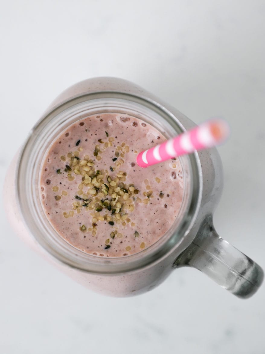 birds eye view of homemade protein shake topped with hemp hearts and pink in colour, with a pink straw inside the jar.