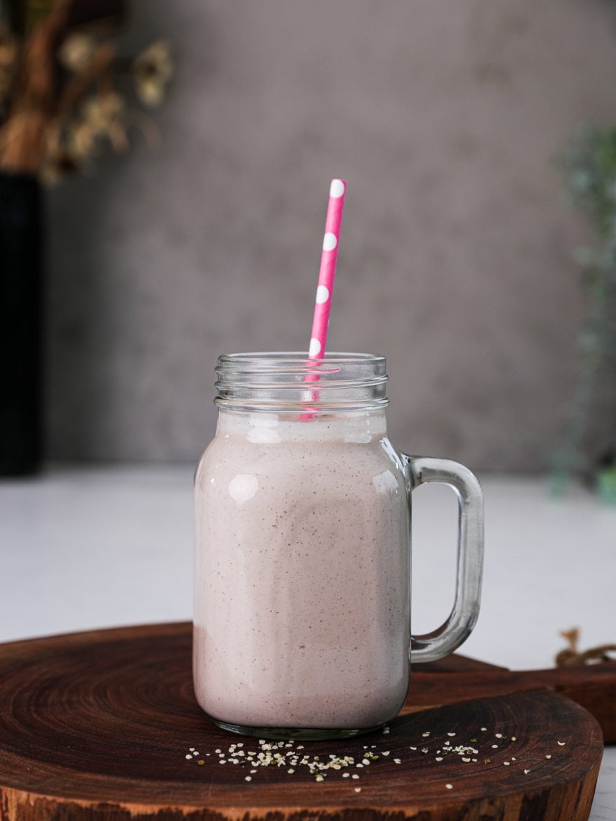 Perspective shot of homemade protein shake on a wooden board with a pink polka dotted straw inside the jar