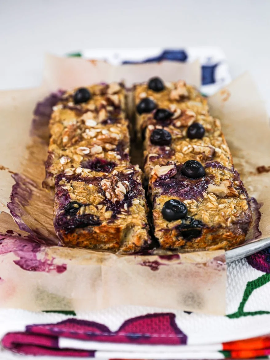 Plate of baked oatmeal squares cut into 6 pieces topped with blueberries and walnuts