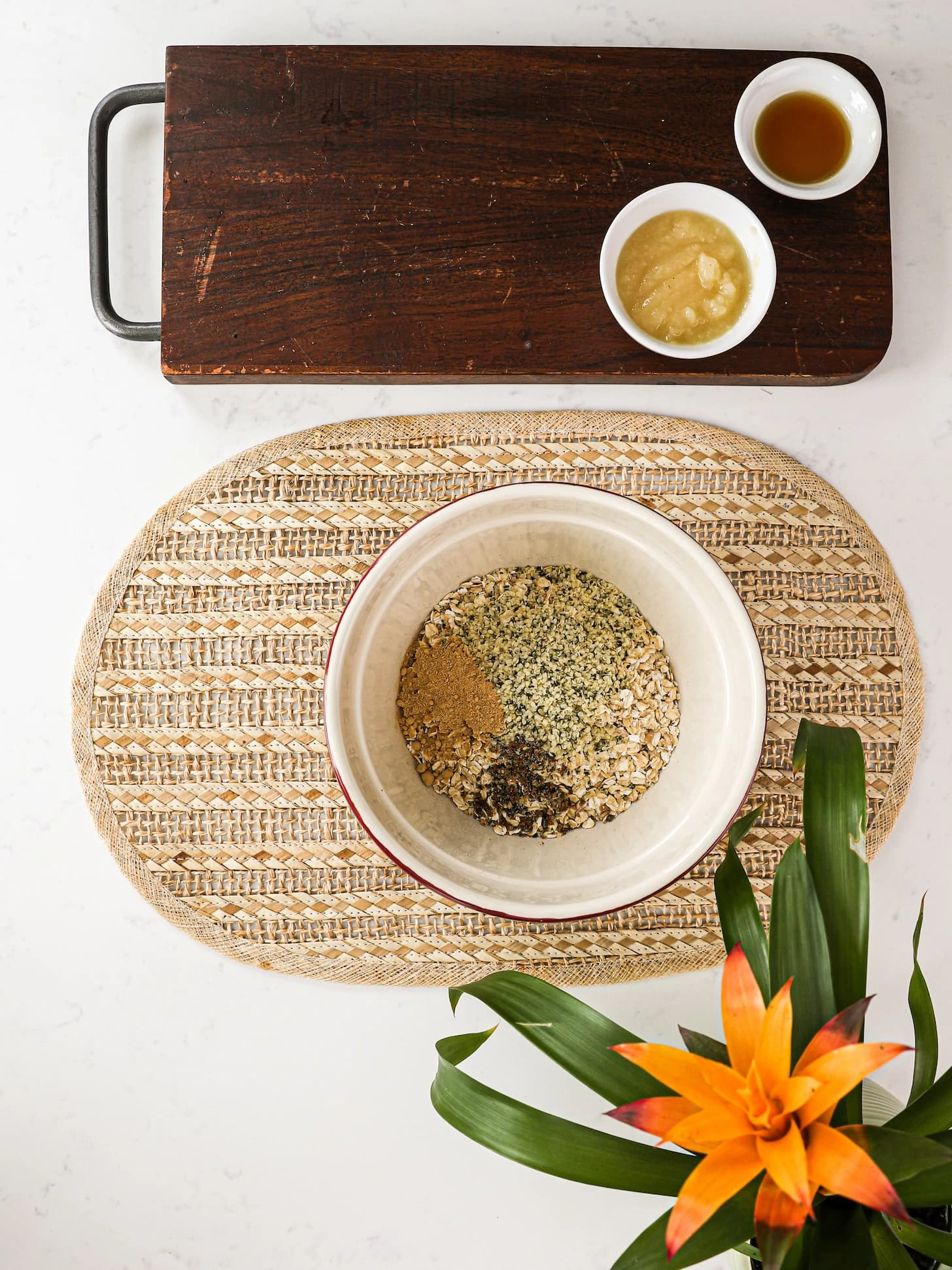bowl of rolled oats, hemp hearts and spices with a wooden board next to it that has apple sauce and maple syrup. There is a plant in the corner.