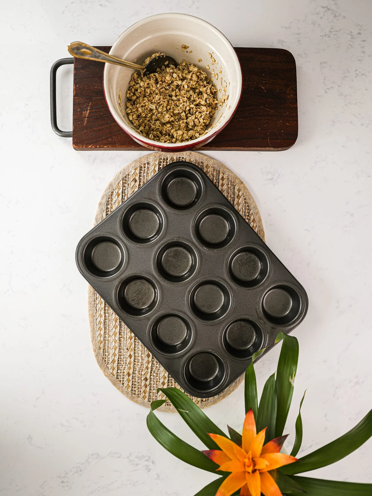 a greased cupcake pan with a bowl of oats next to it. There is also a plant in one corner.