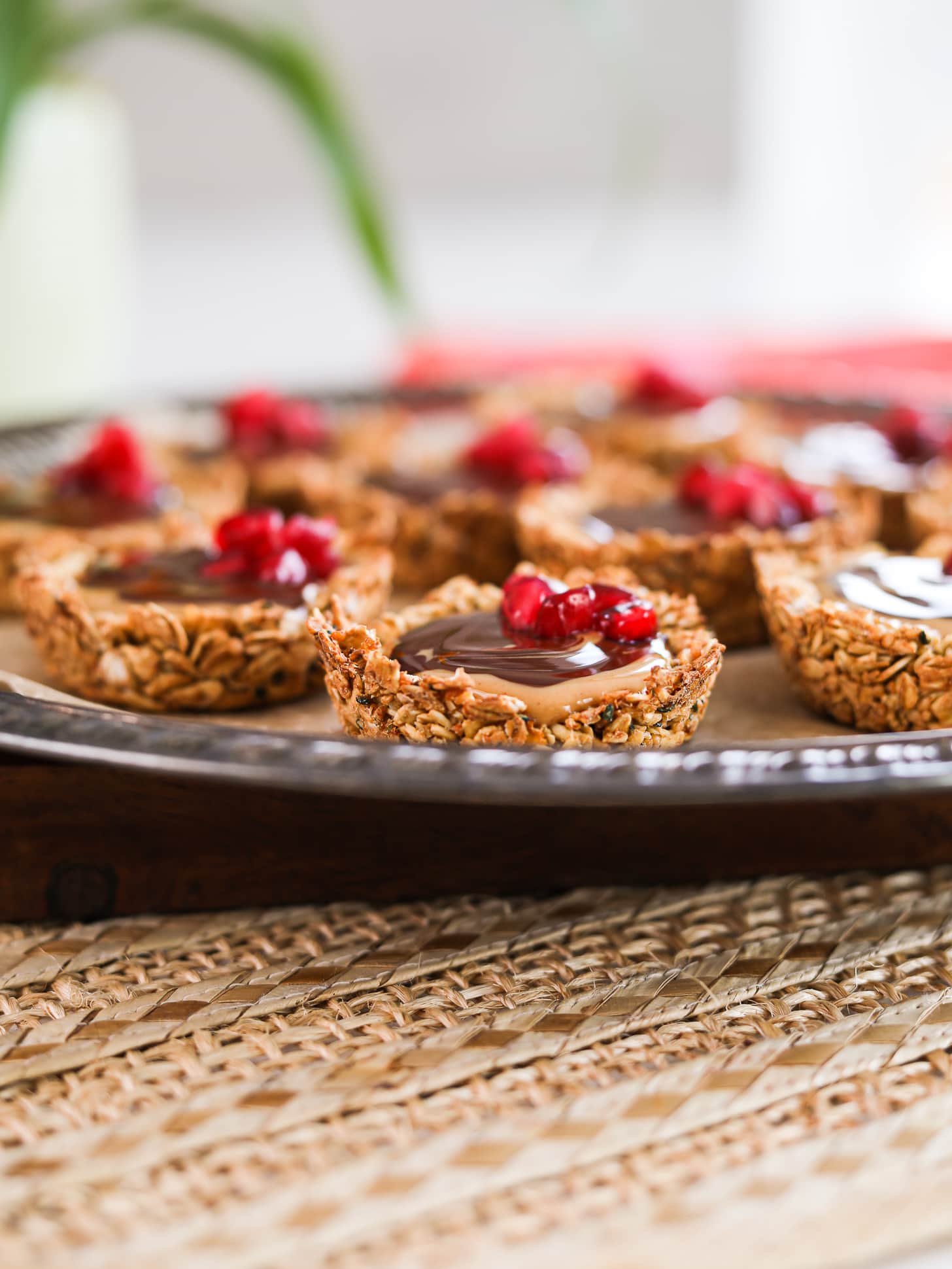 A perspective shot of a tray holding oat cup cookies that are filled with peanut butter and chocolate and topped with pomegranate kernels.