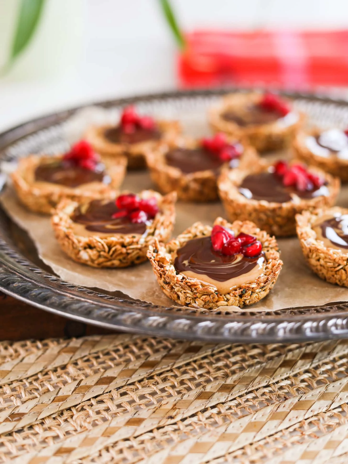 A close up shot of a round tray holding oat cup cookies that are filled with peanut butter and chocolate and topped with pomegranate kernels.