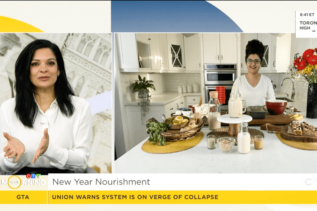 Two women talking; one is in her kitchen surrounded by a display of food and the other is in a television studio.