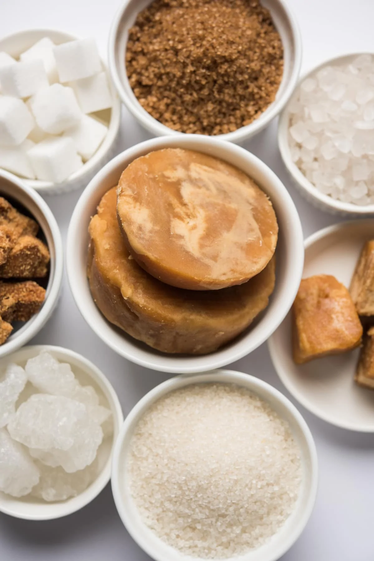 bowls of types of sugars including jaggery, brown sugars, sugar crystals