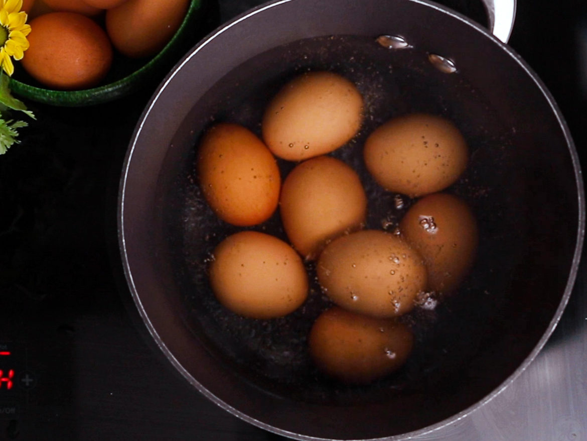 a saucepan filled with water and eggs about to boil on a black stovetop