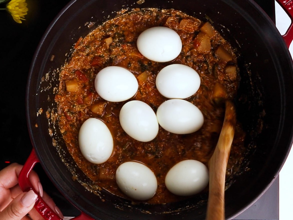 a cooking pot containing eight boiled eggs placed over a tomato turnip curry.