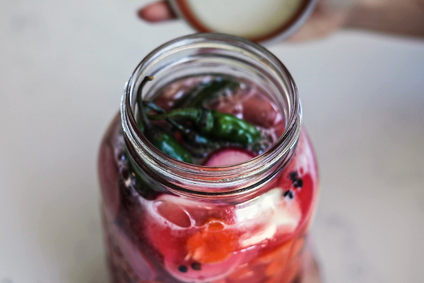 opening of a large mason jar filled with water and vegetables.
