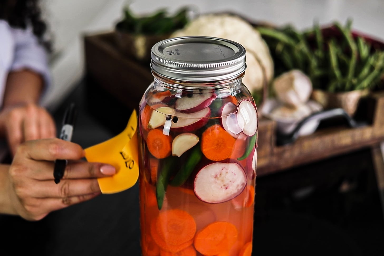 a hand putting a label on a mason jar filled with water and mixed vegetables.