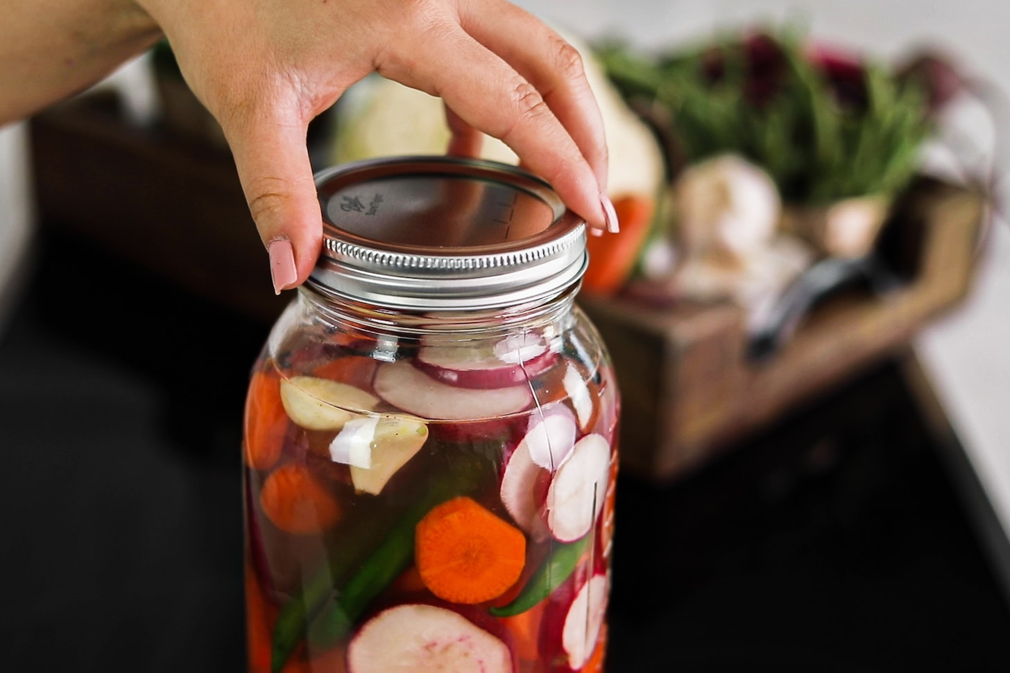 a hand holding the lid of a mason jar filled with water and chopped mixed vegetables.