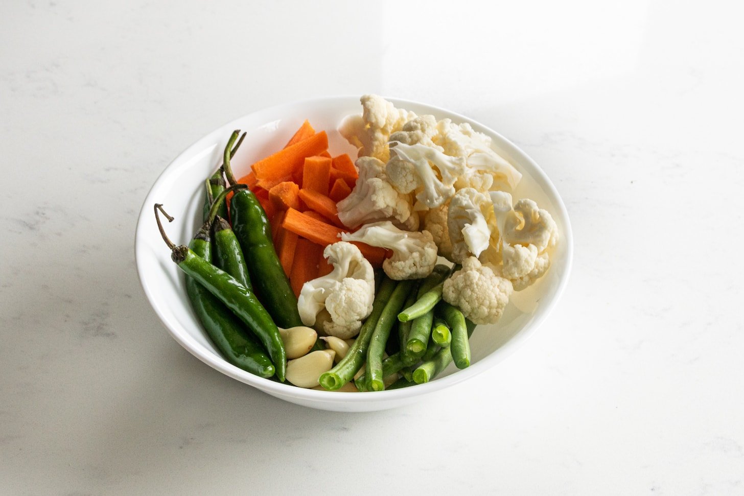 a white bowl of chopped vegetables: carrots, cauliflower, chillies, beans and garlic cloves.