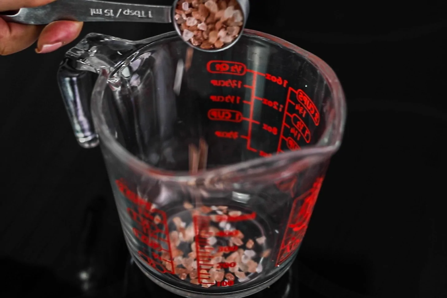 a hand holding a spoon of rock sea salt and adding it to a jug.