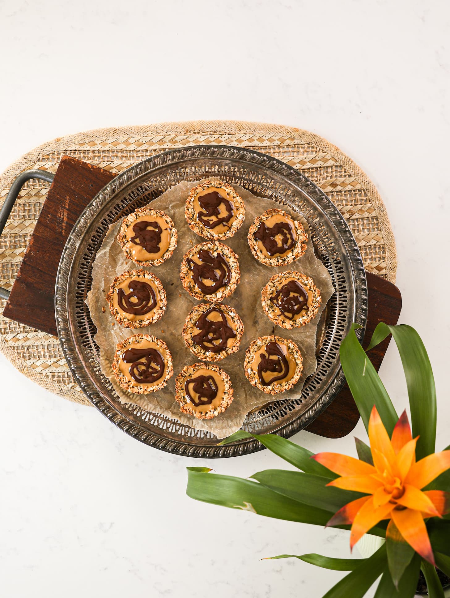 a round tray holding ten oat cups filled with peanut butter and topped with melted chocolate. There is a plant in one corner.