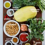 a rectangular wooden board with ingredients for chickpea curry arranged. It includes spaghetti squash, kale, bowl of chickpeas, ramekins of spices, oil, lemon and more.