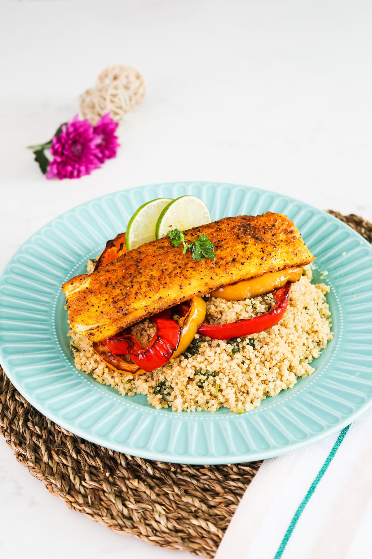 a plate of quinoa topped with roasted pepper rings, pan fried basa fish fillet and lime slices
