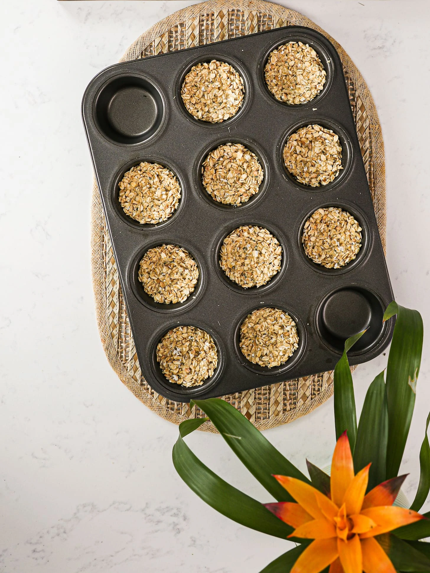 a cupcake pan with oats that have been pressed down to create cups. There is a plant in one corner.