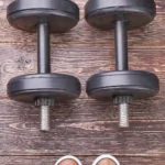 Dumbbells and sneakers, wooden background. Heavy dumbbell and shoes, textured wooden floor.