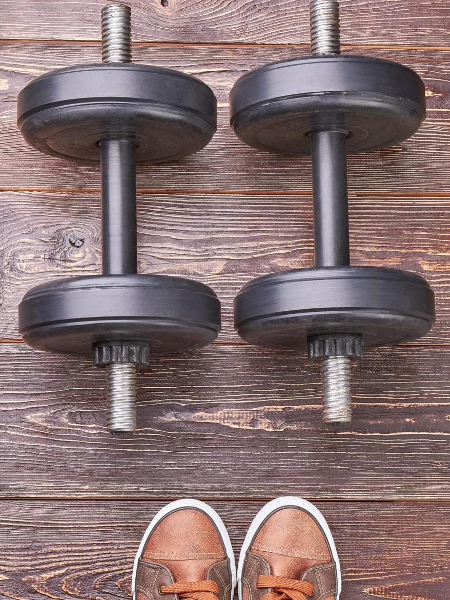 Dumbbells and sneakers, wooden background. Heavy dumbbell and shoes, textured wooden floor.