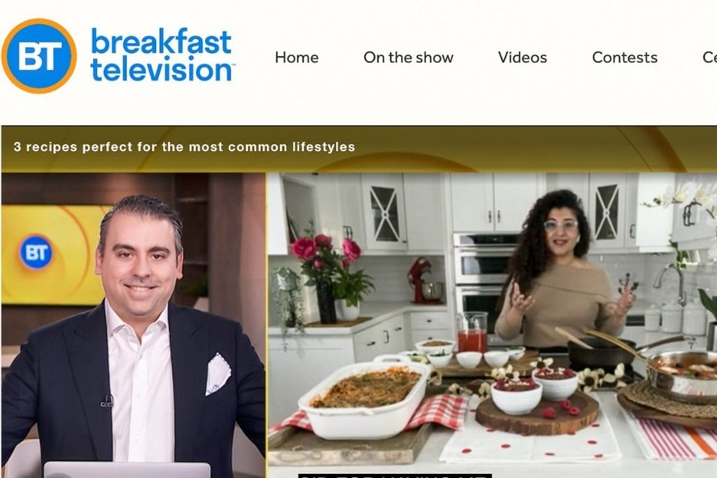 A man and a woman talking; the woman is in her kitchen surrounded by a display of food and the man is in a television studio.