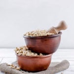 Oat flakes in ceramic bowl and wooden spoon on white vintage wooden background, selective focus copy space, top view