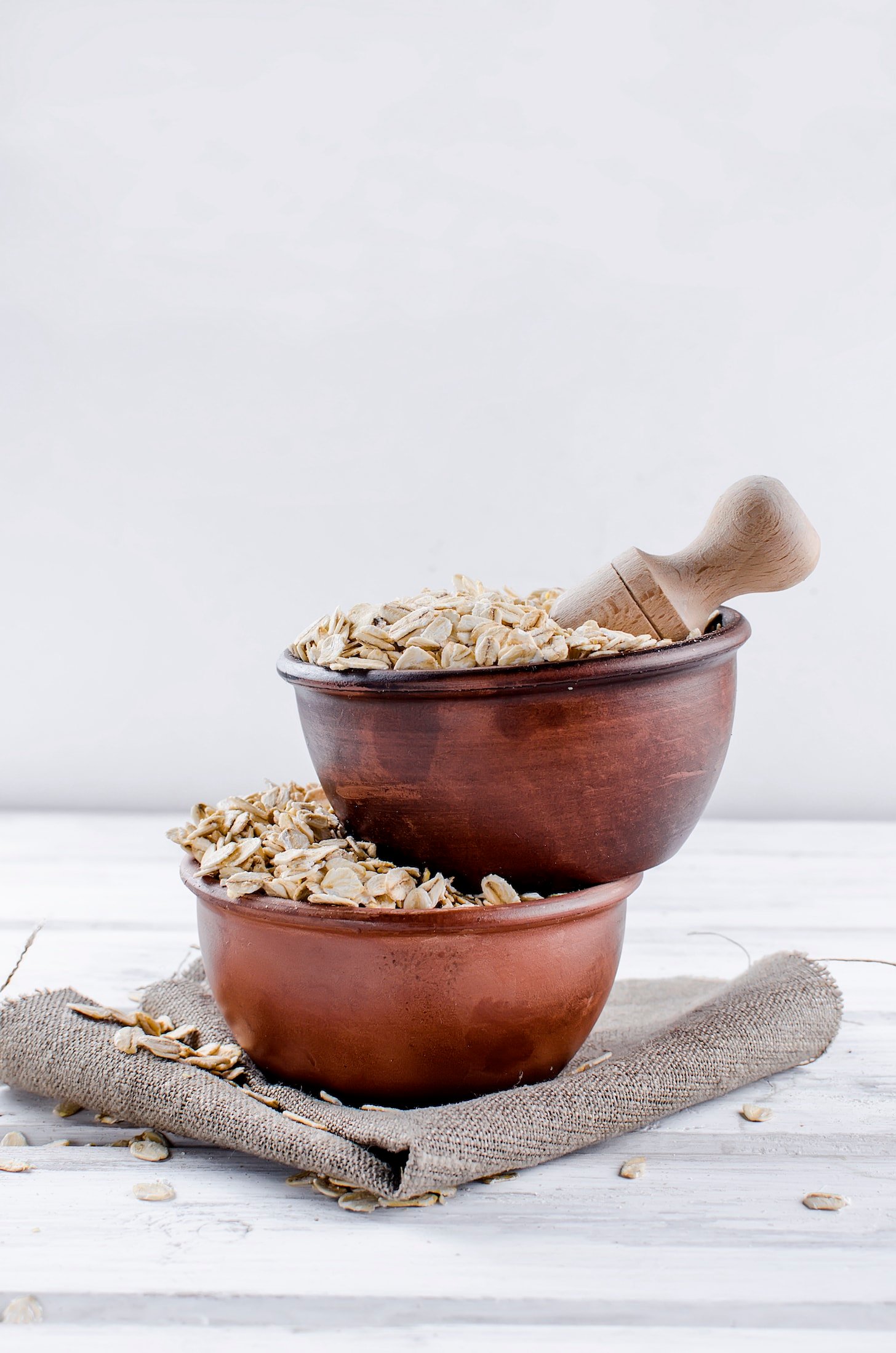 Oat flakes in ceramic bowl and wooden spoon on white vintage wooden background, selective focus copy space, top view