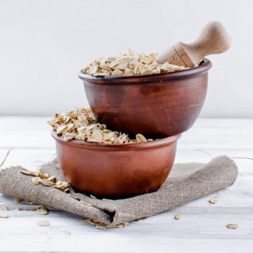 Oat flakes in ceramic bowl and wooden spoon on white vintage wooden background, selective focus copy space, top view