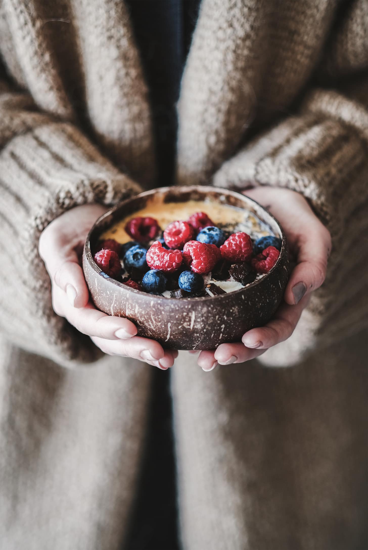 Healthy vegan breakfast bowl. Overnight oats, mango smoothie and fresh berries in coconut shell natural bowl in woman's hands