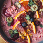 close up shot of pink-coloured oatmeal topped with blood orange segments and chopped blueberries