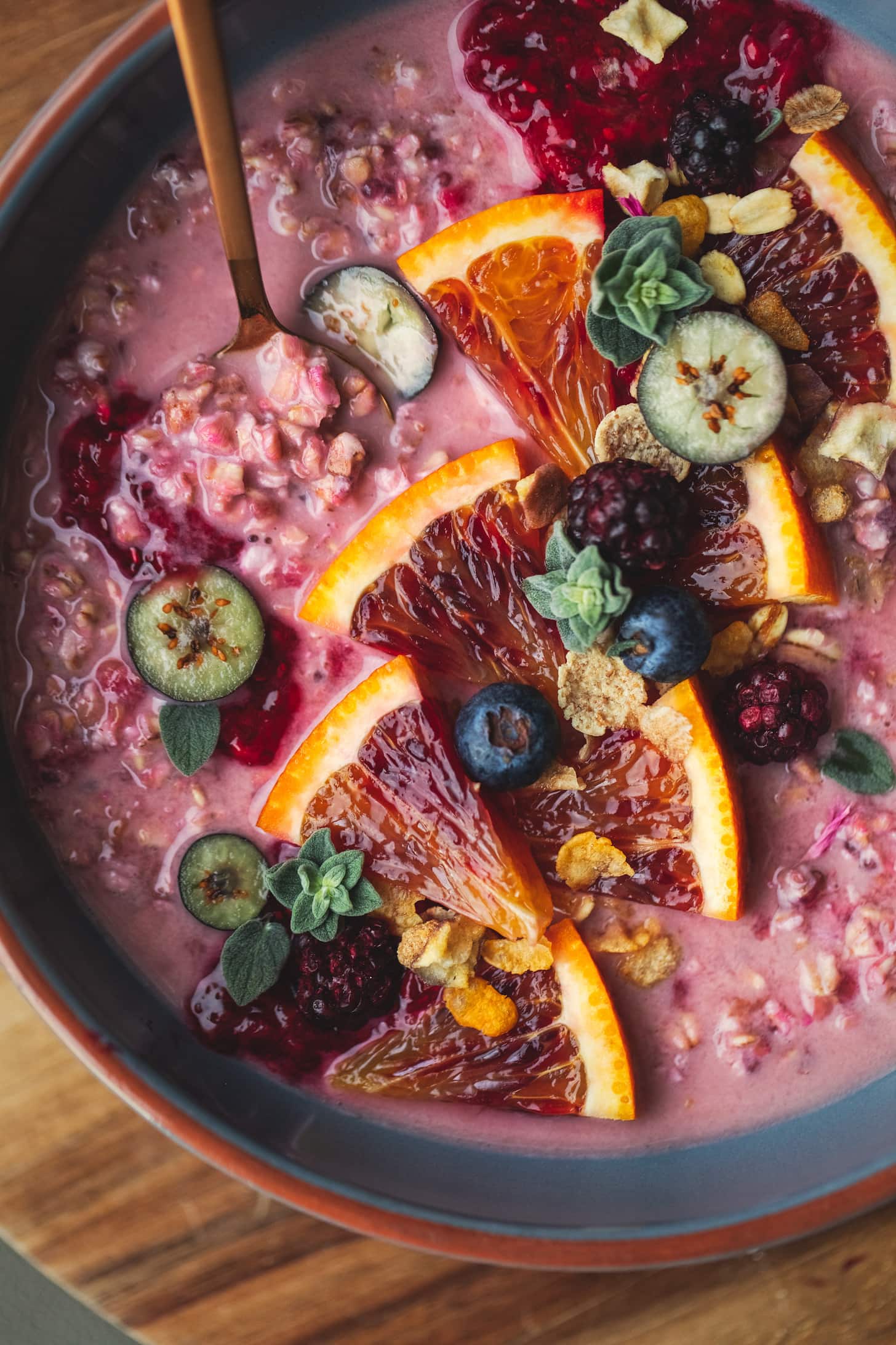 close up shot of pink-coloured oatmeal topped with blood orange segments and chopped blueberries