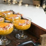 perspective shot of a serving bowls with a thick orange coloured pudding garnished with nuts and dried roses.