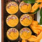 six serving bowls with a thick orange pudding in them garnished with nuts and dried roses placed placed inside a tray with a traditional scarf as decoration.