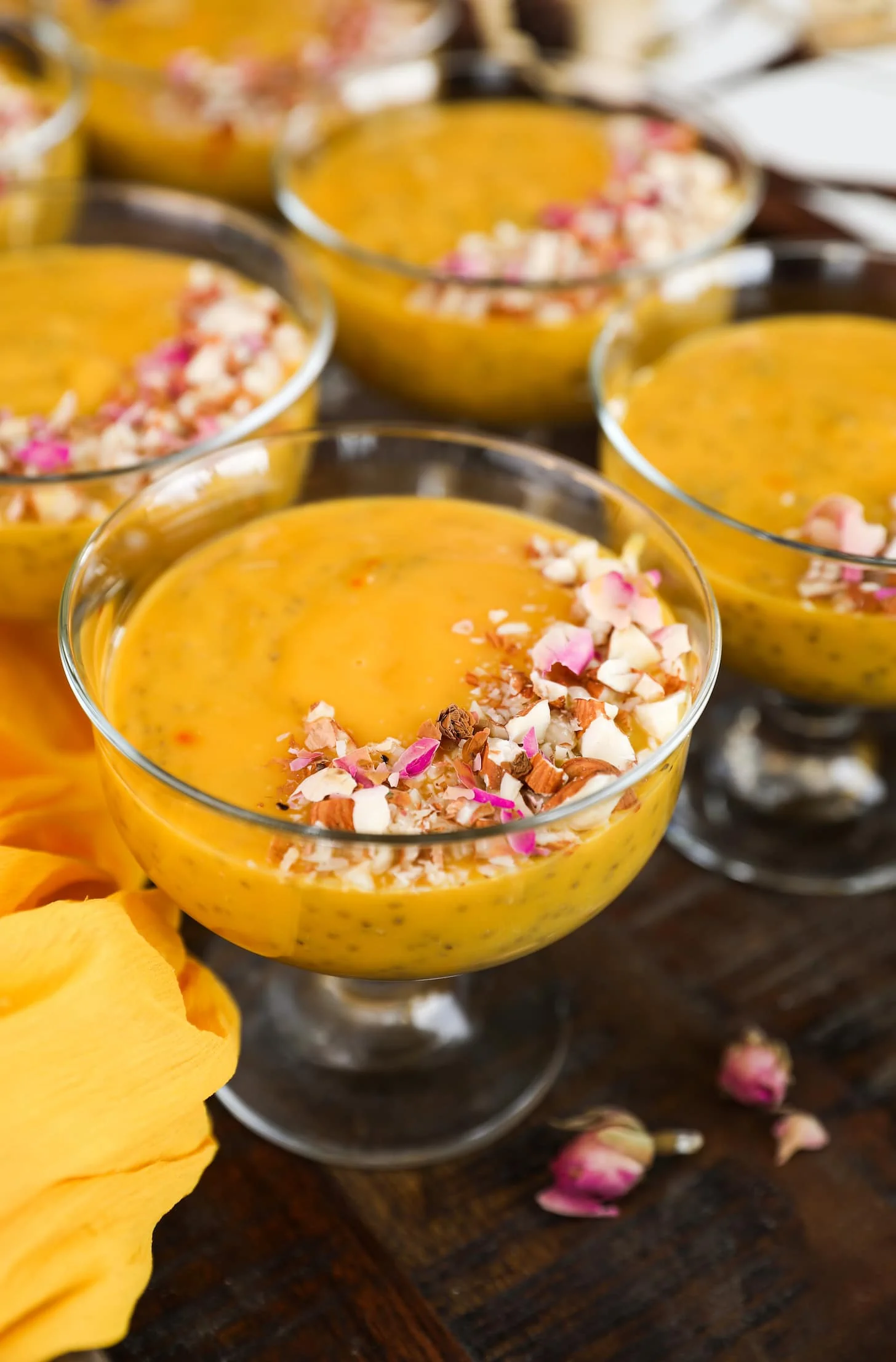 angle shot of a serving bowls with a thick orange coloured pudding garnished with nuts and dried roses.