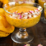 side shot of a serving bowl with a thick orange pudding in it garnished with nuts and dried roses