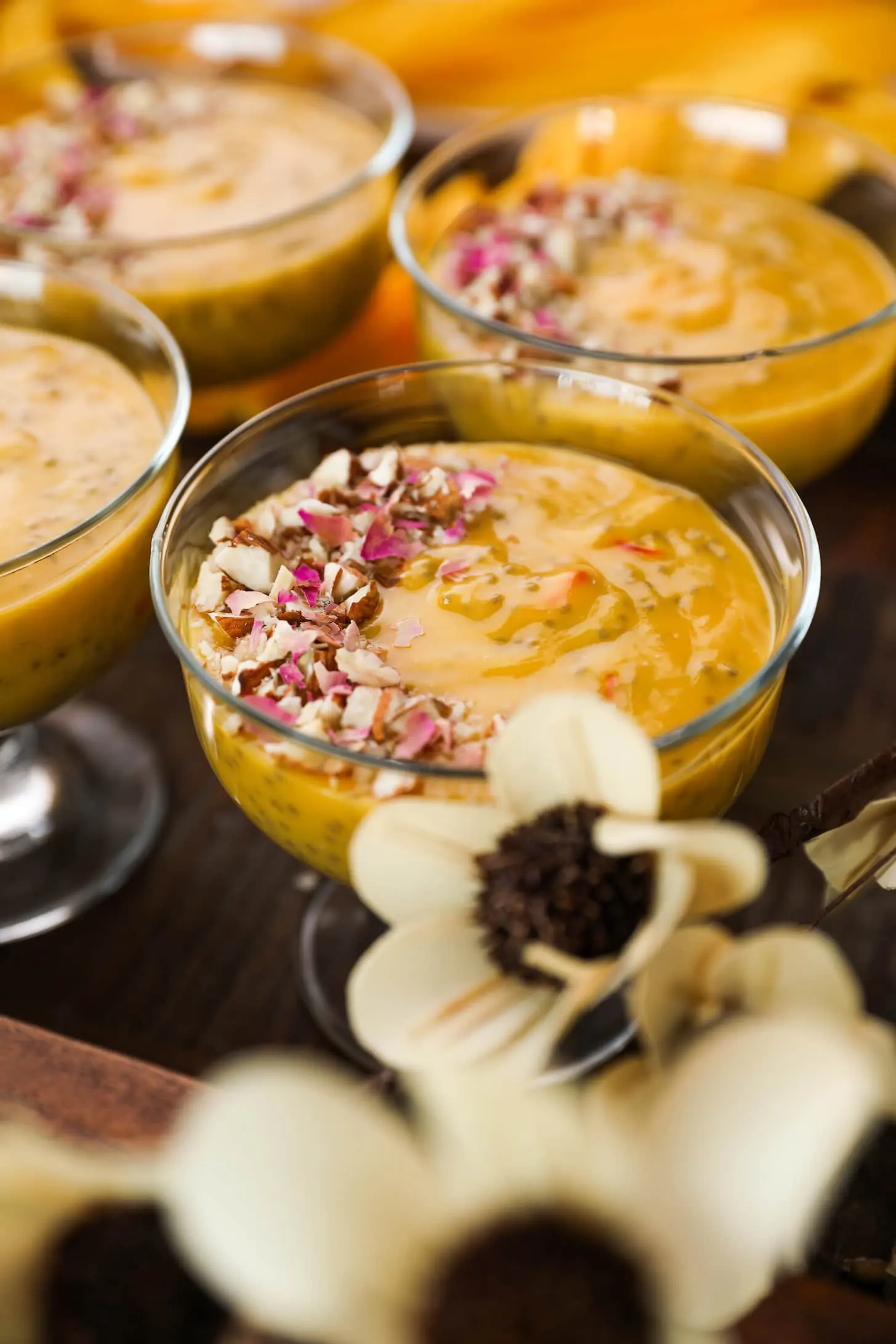 close up shot of a serving bowls with a thick orange coloured pudding garnished with nuts and dried roses.