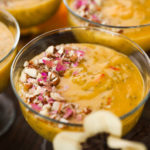 close up shot of a serving bowl with a thick orange coloured pudding garnished with nuts and dried roses.